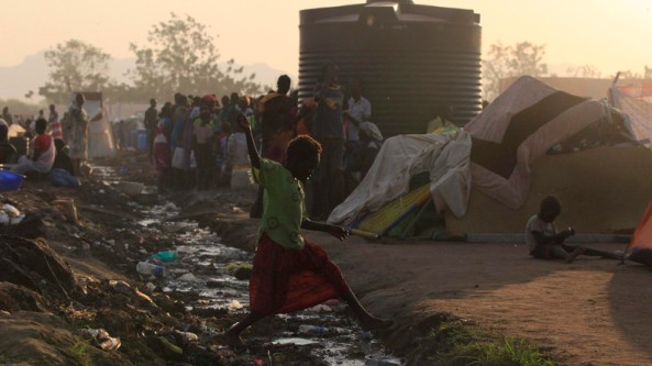 Barefoot girl jumps over an open drain filled with rubbish at Tomping camp in Juba